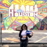 photograh of a woman standing in front of a mural holding a Honduran flag.