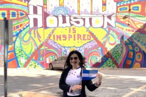 photograh of a woman standing in front of a mural holding a Honduran flag.